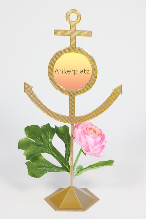 Beispiel-Dekoration - Blumenstecker "Anker silber-goldfarben"  mit Standfuß - an dem Standfuß befestigt ist eine hellrosa Blüte mit einigen Blättern - eingesetztes Foto: gelb-rosafarbener Hintergrund und Text "Ankerplatz"
