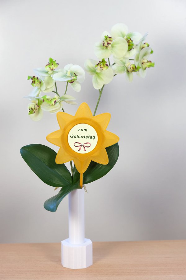 Beispiel-Dekoration - weiße Blumenvase mit weißer Orchidee und  gelbem Blumenstecker "Blume 1" - eingesetztes Foto:  Schleife auf hellem Hintergrund mit Text "zum Geburtstag" und ein Kristallschliff-Stein