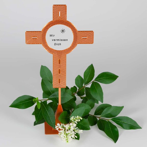 Blumenstecker Kreuz kupferfarben mit einem Aufkleber und dem Schriftzug "Wir vermissen Dich"-dekoriert mit weißen Blüten und grünen Blättern
